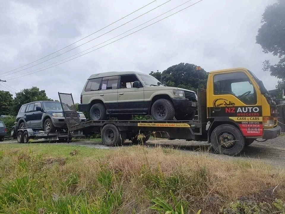 A tow truck carrying two old SUVs during a scrap car removal job in Wellington, showing efficient and professional vehicle towing service.